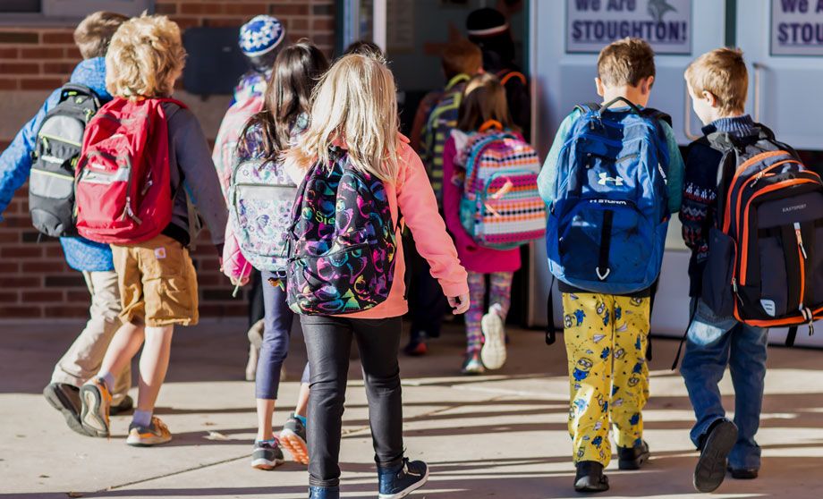 Image of children wearing backpacks walking to school building