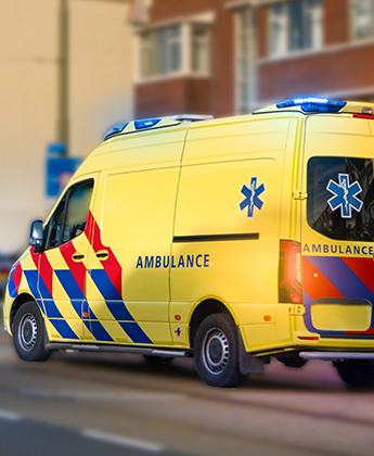 An ambulance vehicle driving in the road with its lights flashing