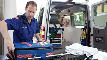 A paramedic is loading a medical bag into an ambulance.