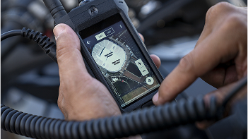 A hand holding a two-way radio with a map screen