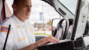 A man in uniform typing on a mounted laptop.
