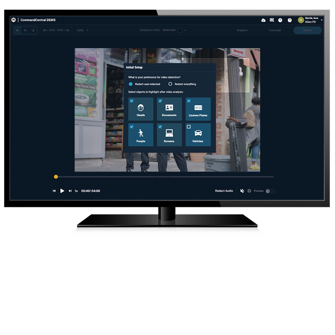  A computer monitor displaying the CommandCentral DEMS interface with an "Initial Setup" modal window overlaid on a video of a street scene. The modal asks, "What is your preference for video detection?" and offers checkable boxes to automatically detect and redact objects including "Heads," "Documents," "License Plates," "People," "Screens," and "Vehicles".