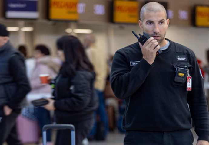 A Belgrade airport employee uses their radio in front of a left item of luggage 