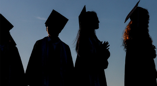 Silhouette of four college graduates in cap and gown
