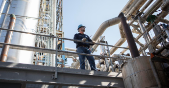 Worker stands in an oil and gas facility holding a MOTOTRBO radio. 