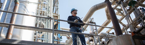 Worker stands in an oil and gas facility holding a MOTOTRBO radio. 