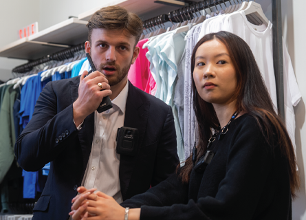 Retail employees standing side by side, employee on the left speaking in to radio