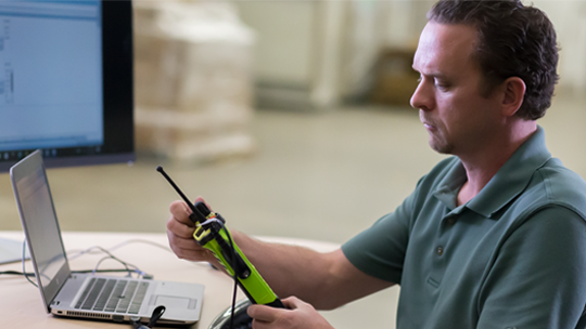 Man examining radio while sitting in front of computer