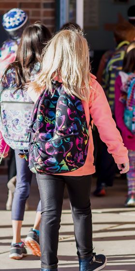Image of children wearing backpacks walking to school building