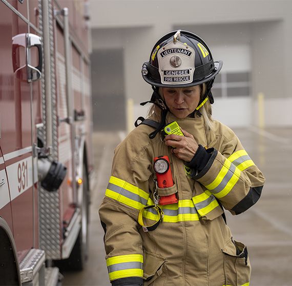 Image of woman firefighter next to red fire truck talking into a Motorola Solutions device