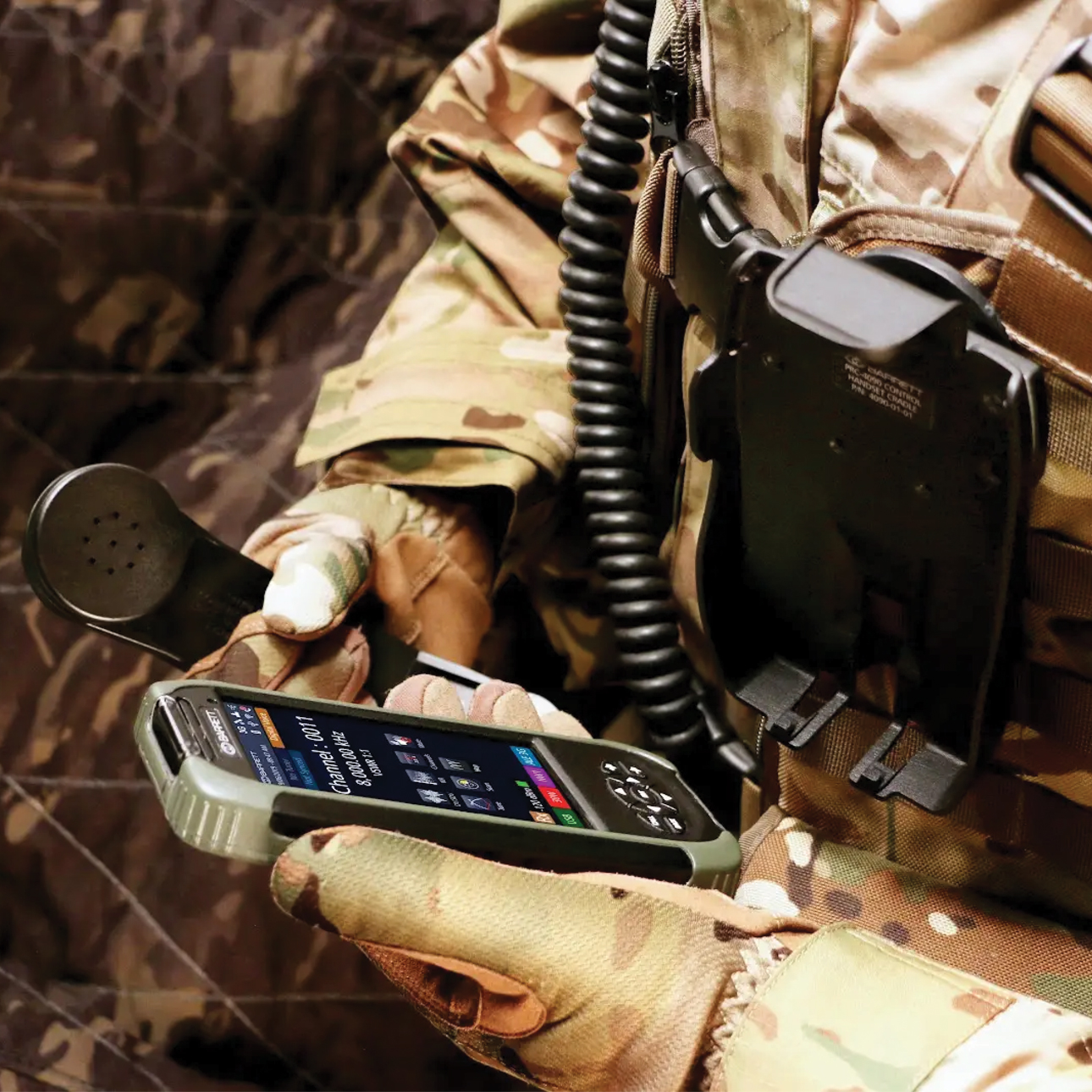PRC-4090 control handset in hand, cradle on webbing visible