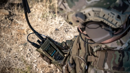 Person in military fatigues holding a PRC-4080 radio