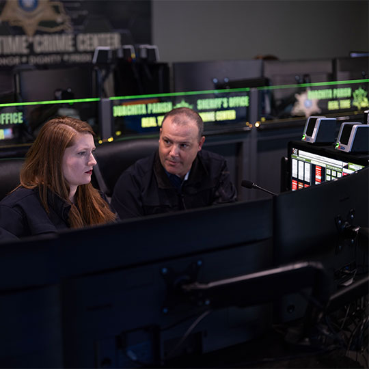 Two operators at a real-time crime center consult with each other to resolve an incident in progress
