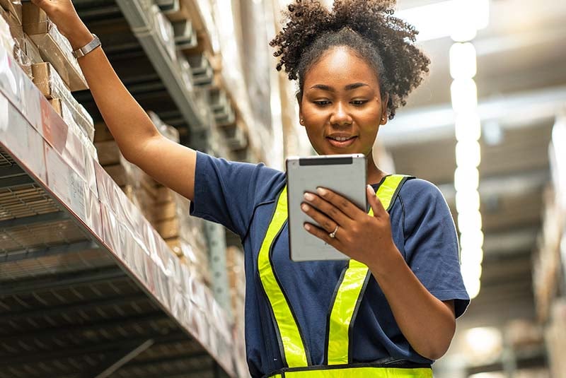 A happy business owner in a stock room, checking their inventory on a tablet.