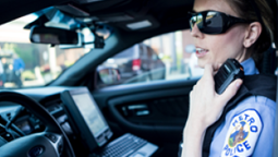 ASTRO P25 Radio Systems Police officer inside car keying up and speaking into shoulder-worn radio