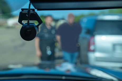 Photo of a dashboard camera in a police car. Through the window you can see a man being arrested,