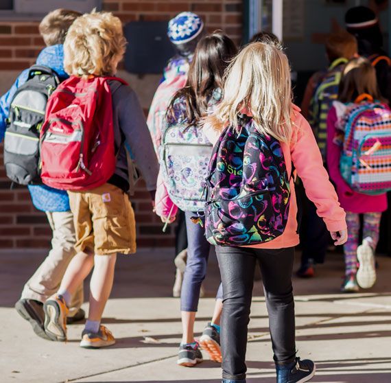 Image of children wearing backpacks walking to school building